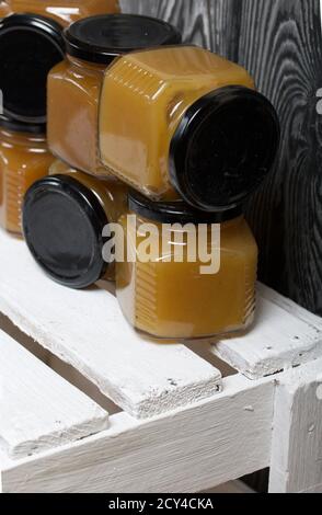 Obstkonfitüre in Gläsern. Steht auf einer weiß bemalten Holzkiste. Vor dem Hintergrund von schwarzen Kieferntafeln. Stockfoto