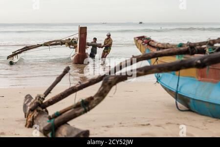 Weligama, Sri Lanka - 21. Dezember 2017: Sri-lankische Fischer schieben das Boot morgens nach der Fischernacht in Sri Lanka ins Meer. Stockfoto