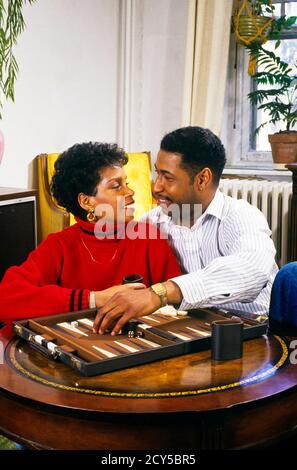 1990S ROMANTISCHES AFROAMERIKANISCHES PAAR SPIELT BACKGAMMON - KS36321 NET002 HARS LIFESTYLE FRAUEN VERHEIRATET EHEPARTNER EHEMÄNNER ZU HAUSE LEBEN KOPIEREN RAUM FREUNDSCHAFT HALB-LÄNGE DAMEN PERSONEN PFLEGE MÄNNER VERTRAUEN PARTNER AUS TRÄUME FRÖHLICH HIGH-ANGLE AFRO-AMERIKANER AFRO-AMERIKANISCHE SCHWARZE ETHNIE ATTRAKTION BEZIEHUNGEN LÄCHELT WERTIGKEIT KONZEPTIONELLE FRÖHLICH STILVOLLE PERSÖNLICHE BINDUNG MÖGLICHKEIT ZUNEIGUNG BRETT SPIEL ZUSAMMENARBEIT EMOTION SOZIALE AKTIVITÄT ZWEISAMKEIT FRAUEN JUNGER ERWACHSENER MANN JUNGER ERWACHSENER FRAU UMWERBEN ALTMODISCHE AFROAMERIKANER Stockfoto