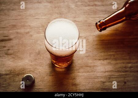 Liegende Bierflasche, Flaschendeckel und Glas mit Bier auf Holzhintergrund Stockfoto