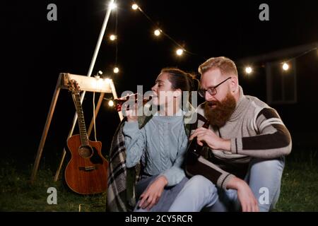 Freunde, die Spaß am Abend Picknick mit Getränken. Junge kaukasische Paar beim bbq auf dem Land Stockfoto