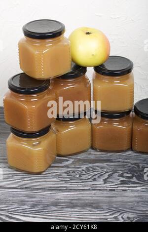 Marmelade in Gläsern. Es gibt einen Apfel in der Nähe. Auf schwarzen Kiefernbrettern. Stockfoto