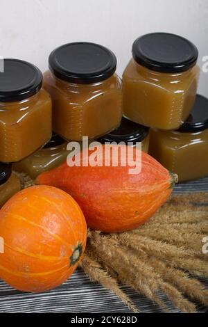 Marmelade in Gläsern. In der Nähe ist ein Kürbis und ein Strauß von trockenem Gras mit Dornen. Auf schwarzen Kiefernbrettern. Stockfoto