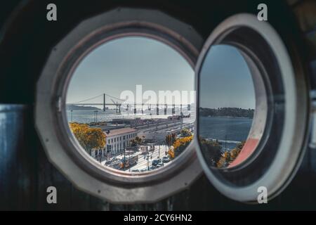 Blick durch das runde Fenster eines antiken Hauses von Lissabon Stadtbild im Hintergrund mit der Brücke über den Tejo, Straße mit alten Straßenbahnen, und Stockfoto