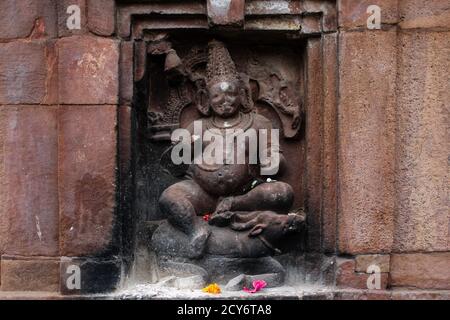 Eine braun gravierte hinduistische Skulptur mit einer gelben und einer rosa Blume vor dem Brahmesvara Tempel in Bhubaneswr, Odisha, Indien Stockfoto
