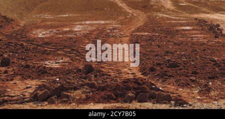 Großes Stockbild einer roten sandigen staubigen Straße mit Reifenspuren, die wie der Planet Mars aussehen. Selektiver Fokus auf die Bildmitte. Stockfoto