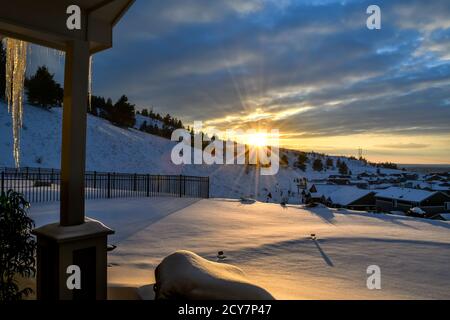 Blick von der Terrasse eines Hauses, während die Sonne hinter einem Hügel über einer Unterteilung von Häusern während Schnee und Winter in Spokane, Washington USA untergeht Stockfoto