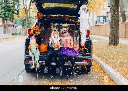 Trick or Trunk. Kinder feiern Halloween im Kofferraum des Autos. Junge und Mädchen mit roten Kürbissen feiern traditionelle Oktober Urlaub im Freien. Sozial Stockfoto