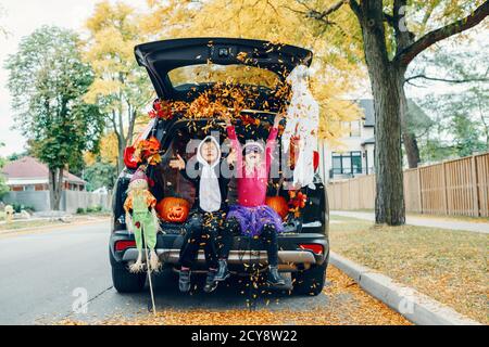Trick or Trunk. Kinder feiern Halloween im Kofferraum des Autos. Junge und Mädchen mit roten Kürbissen feiern traditionelle Oktober Urlaub im Freien. Sozial Stockfoto