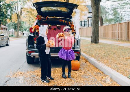 Trick or Trunk. Kinder feiern Halloween im Kofferraum des Autos. Junge und Mädchen mit roten Kürbissen feiern traditionelle Oktober Urlaub im Freien. Sozial Stockfoto