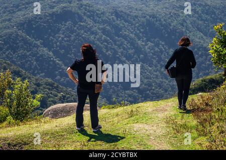 Touristen wandern und betrachten die Aussicht auf der gegenüberliegenden Seite des Pedra da Macela Wahrzeichen, im Serra da Bocaina Nationalpark. Stockfoto