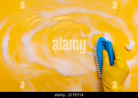 Wischen Sie den Schaum auf einem gelben Hintergrund mit einem blauen Handpinsel ab. Stockfoto