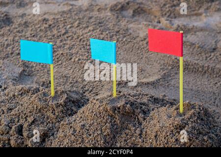 Im Sandkasten drei Sandhügel von links nach rechts mit zwei blauen Fahnen auf der linken und roten Flagge auf der rechten Seite. Konzept: Führung in der Geschäftsstrategie Stockfoto