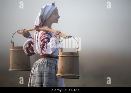 Besticktes Hemd und Eimer auf den Schultern einer jungen attraktiven Frau. Stockfoto