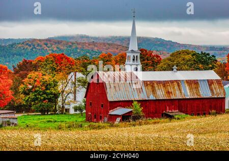 Woodstock, Vermont - Oktober 8, 2018 - Rote Scheune und Kirche neben einem Abgeernteten cornfiield mit herbstlichen Farben im Hintergrund Stockfoto