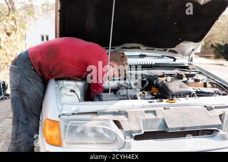 Das Konzept der Behinderung von Menschen und ihre Anpassung an das Leben. Ein behinderter Mann repariert den Motor des Autos, man kann die Hände nicht sehen. Deaktiviert fr Stockfoto