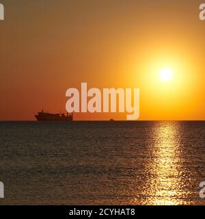 Sonnenuntergang am wolkenlosen Himmel auf dem Meer, Schiffe stehen am Horizont. Stockfoto