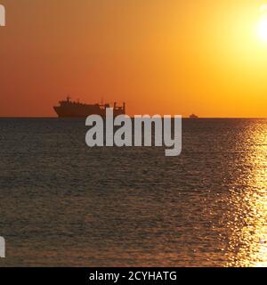 Sonnenuntergang am wolkenlosen Himmel auf dem Meer, Schiffe stehen am Horizont. Stockfoto