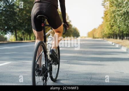 Mann auf einem Schotterrad auf der Straße, Rückansicht. Beine eines Radfahrers, der ein modernes Fahrrad im Freien fährt Stockfoto