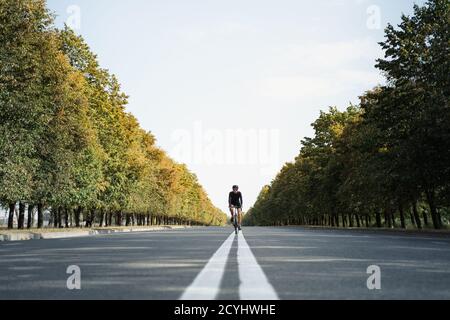 Mann fährt ein Schotterrad in der mittleren Spur der Straße. Gut ausgerüsteter Radfahrer auf einem modernen Fahrrad im Freien, symmetrisches Bild Stockfoto