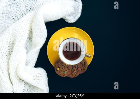 Weiß gestrickt Stoff, Porzellan Gold Tasse mit Kaffee und gelben Teller mit aromatisierten Cookies mit farbigen Tropfen auf schwarzem Hintergrund. Handwerk auf schwarzem Bac Stockfoto