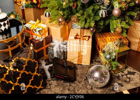 Weihnachtsbaum mit goldenen Kugeln verziert. Unter dem Weihnachtsbaum eine große Anzahl von Weihnachtsgeschenken. Weihnachtsfeiertagskonzept. Eine riesige Anzahl von Geschenk Stockfoto