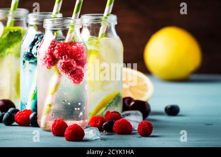 Beeren, Früchte und Zitrusfrüchte alkoholfreie kalte Getränke und Cocktails in Glasflaschen auf blauem Hintergrund, Kopierraum Stockfoto