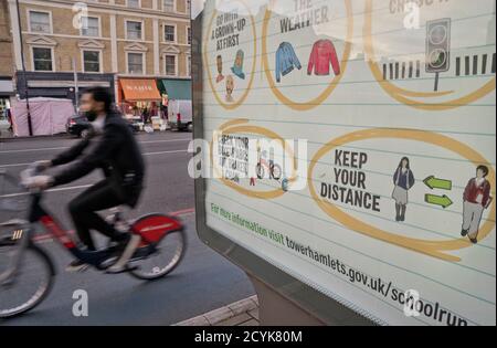 Anwohner radeln in Whitechapel, mit Schildern, die darauf hinweisen, dass sie aufgrund der Coronavirus/Covid-19 Pandemie in London, England, Großbritannien, in sicherer sozialer Distanz bleiben sollten Stockfoto