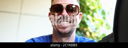 Mann in Sonnenbrille sitzt und lächelt ganz in der Nähe Stockfoto
