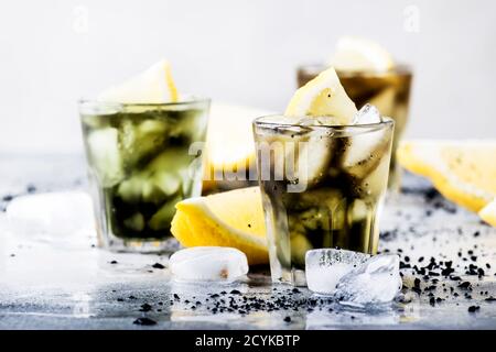 Gesundes Essen und Trinken Konzept: eistickes schwarzes Detox-Limonadenwasser mit zerkleinerten Eis- und Zitronenscheiben in Gläsern, Aktivkohle, grauer Hintergrund, tre Stockfoto