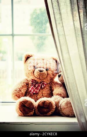 Braune Teddybären am Fenster an einem regnerischen Tag, getöntes unscharfes Bild, selektiver Fokus Stockfoto