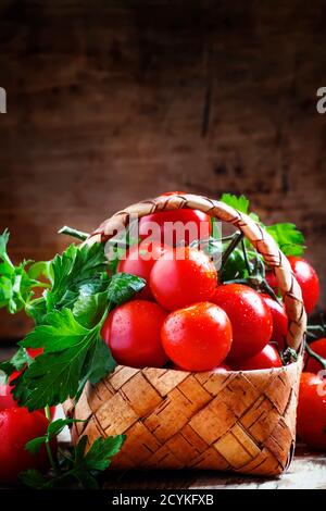 Kirschtomaten und Petersilie im Korbkorb auf einem alten Holztisch im rustikalen Stil, selektiver Fokus Stockfoto