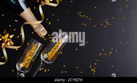 Weihnachtliche Champagnerflasche und Gläser mit goldenem Konfetti und Dekorationen auf schwarzem Hintergrund. Flach liegend, Draufsicht, Kopierbereich. Bannermockup, greeti Stockfoto