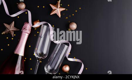 Elegante Weihnachtskomposition mit Rosé-Weinflasche, Sektgläsern, Kugeln Dekorationen, Sternen, Konfetti auf schwarzem Hintergrund. Flach liegend, Draufsicht. Ch Stockfoto