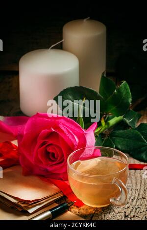 Vintage Postkarte mit Tasse Kräutertee, ein Päckchen alte Buchstaben, gebunden mit einem Band, rosa Rose, Kerzen auf dem alten Holzhintergrund, selektiv Stockfoto