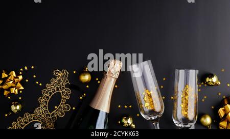 Weihnachtsfeier Konzept. Flache Lay-Komposition mit Champagnerflasche, Gläsern, goldenen Dekorationen, Bällen, Karnevalsmaske auf schwarzem Hintergrund. Draufsicht. Stockfoto