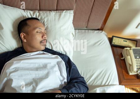Draufsicht auf den asiatischen Mann, der in seinem weißen Bett schläft Zu Hause Stockfoto