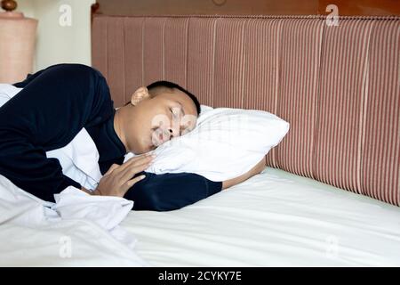Seitenansicht des asiatischen Mannes, der in seinem weißen Bett schläft Zu Hause Stockfoto
