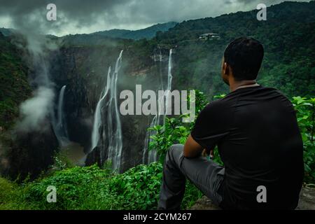 Mann, der am Felsen sitzt und den wunderschönen Wasserfallstrom lang beobachtet Die am Abend aufgenommene Belichtung wird in einem abgelegenen Western aufgenommen ghat Wälder karnataka indi Stockfoto