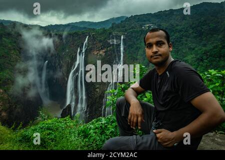 Mann, der am Felsen sitzt und den wunderschönen Wasserfallstrom lang beobachtet Die am Abend aufgenommene Belichtung wird in einem abgelegenen Western aufgenommen ghat Wälder karnataka indi Stockfoto
