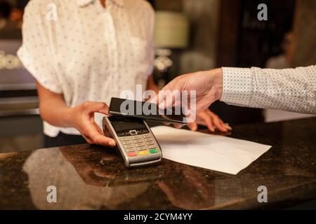 Eine nicht erkennbare weibliche Hotelrezeption, die die kontaktlose Bezahlung eines Kunden nimmt, der im Hotel eincheckt, benutzt er sein Smartphone Stockfoto