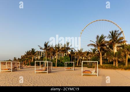 Dubai, VAE, 06/09/20. Sandstrand in Dubai, mit Doppel-Sonnenliegen, Dubai Eye Riesenrad und Palmen im Hintergrund, goldene Stunde. Stockfoto