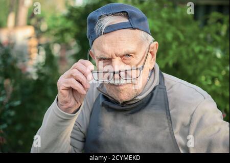 Müder alter Mann sieht seinen Gesprächspartner an, stellt seine Brille ein. Der alte Mann kann ohne Brille nicht sehr gut sehen. Stockfoto