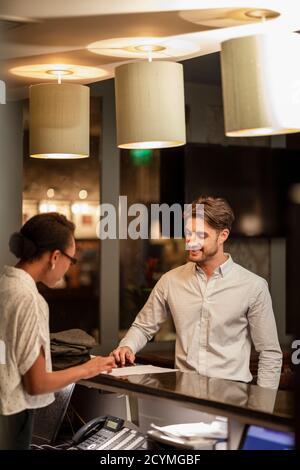Ein Rezeptionist des Hotels, der mit einem Gast spricht, der im Hotel eincheckt. Stockfoto