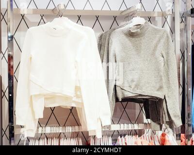 Graue und weiße Pullover hängen an Kleiderbügeln im Laden Stockfoto