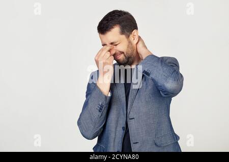 Junger Geschäftsmann Mann mit Bart in einer Jacke, müde von Reiben seine Nase und Hals, Gefühl müde und Kopfschmerzen. Stress und Frustration Konzept. Porträt eines Mannes auf grauem Hintergrund. Stockfoto