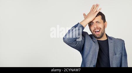 Junger Geschäftsmann Mann mit einem Bart in einer Jacke, Panik wegen einer vergessenen Frist, legte seine Hand auf den Kopf für einen Fehler fühlt sich Stress, gezwungen, das Chaos oder Fehler zu vertuschen. Grauer Hintergrund Stockfoto