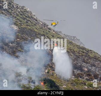 Ein Feuerwehrhubschrauber, der Wasser auf einem Fynbos-Wildfeuer ablässt Südafrika Stockfoto