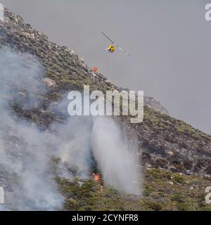 Ein Feuerwehrhubschrauber, der Wasser auf einem Fynbos-Wildfeuer ablässt Südafrika Stockfoto