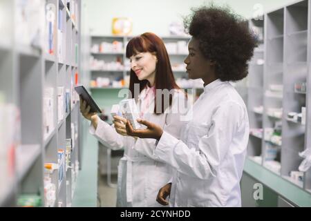 Medizin, Pharmazie, Gesundheitswesen und Menschen Konzept. Zwei junge multiethnische Apothekerin, afrikanische und kaukasische, Einnahme von Medikamenten aus der Stockfoto